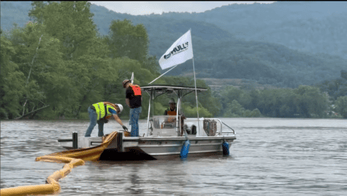 two oil spill response technicians deploy 18 inch containment boom into the water for oil containment and recovery